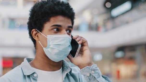 Close-up African American guy in medical face protective mask talking mobile phone answering call talks to doctor remotely complaining about coronavirus symptoms business conversation with smartphone — Video