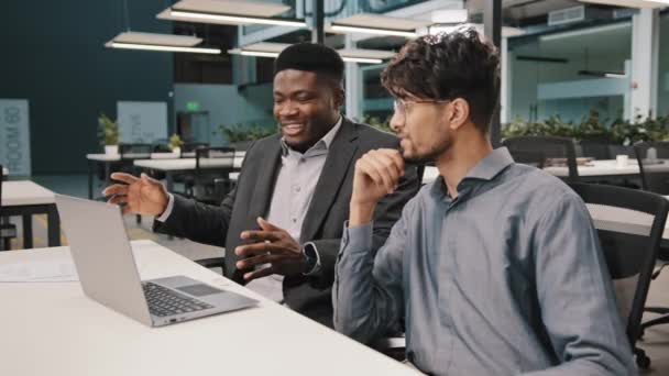 Side view diverse happy mates men african businessman talking with arabian worker having fun together nice conversation multiracial young people comworkers laugh joke at office — Wideo stockowe