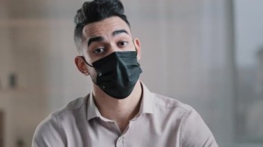 Arap işadamı maske takıyor. Ofis masasında oturuyor. El sallıyor, işaret parmağı sallıyor. Hastalık belirtileri gösteriyor.