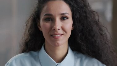 Güzel, genç, kadın, bin yıllık kıvırcık saçlı, ofis çalışanlarına poz veren, mutlu, profesyonel, etnik çeşitlilik gösteren, yakından gülümseyen bir öğrenci.