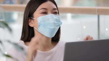 Medikal koruyucu maske takan başarılı Asyalı kız dizüstü bilgisayara bakan kadın, Covid 'in kazanma işinden geri dönüş bildirimi aldı.