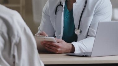 Yakın plan erkek, kimliği belirsiz doktor üniformalı adam masa başında oturup hasta şikâyetlerine danışır stajyer hekime tedavi programı el yazısını açıklar mısın?