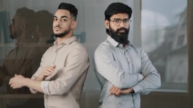 Çok ırklı çiftler iş arkadaşları erkek iş arkadaşları gözlüklü Arap sakallı adam içeride kameraya bakan ciddi bir ifadeyle çapraz kollar. 