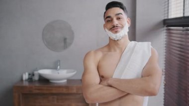 Yakışıklı, kendine güvenen, 30 'lu yaşlarda, kaslı, erkek otel banyosunda beyaz köpüklü tıraş jölesiyle kameraya bakıyor.