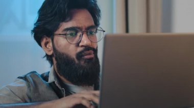 Yakın plan, meşgul, sakallı, İspanyol asıllı Hintli, 35 'lik adam dizüstü bilgisayara bakıyor, internette haberleri okuyor, internet sitelerinde geziniyor, e-postaları kontrol ediyor, internet mağazasında satın alma kararı veriyor.