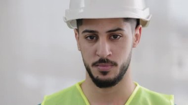 Yakın plan portre ciddi İspanyol müteahhit tamirci erkek müteahhit özel üniformalı güvenlik kaskı takıyor ve kendine güvenen Arap mühendis ustabaşına bakıyor.