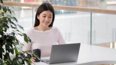 Asyalı kız öğrenci kafede bilgisayarlı iş kadını serbest gazeteci programcıyla birlikte internetten öğreniyor kafeteryada oturmuş kahve içiyor dizüstü bilgisayar yazarak uzaktan çalışma projesi yapıyor.