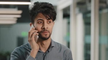 Gülümseyen Arap genç, çok ırklı iş adamı iş yerinde cep telefonunu arıyor İspanyol çalışan satıcı kapalı alanda yapılan konuşmaları tartışıyor cep telefonuyla müşteriye danışmanlık yapıyor.