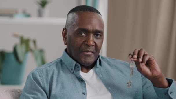 Portre olgun Afro-Amerikan erkek mutlu ev sahibi yeni dairenin anahtarlarını gösteriyor kamera emlakçısına bakıyor ev kredisi satıyor modern konut geliştirme satın alıyor. — Stok video