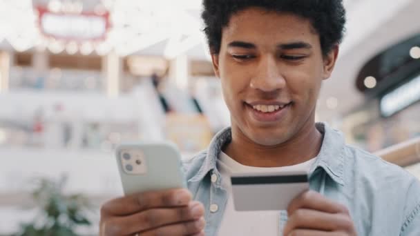 Primer plano hombre africano hace la compra en las tiendas en línea de Internet aplicación de uso de tarjetas de crédito de plástico y teléfono celular. Aplicación de tecnología moderna chico reserva hotel compra pago a distancia smartphone — Vídeos de Stock