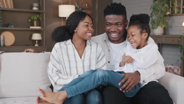 Familia afro-americană stând pe canapea acasă în camera de zi vorbind conversație ocazională râzând timp fără griji împreună părinții vorbesc cu fiica fată copil amuzant chat comunicare glumă distracție — Videoclip de stoc