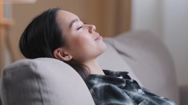 Side view close up Asian calm woman relaxed Korean lady in checkered casual shirt close eyes resting sleep on back of couch relaxing dreaming on comfortable sofa in living room at home lazy time — Vídeos de Stock