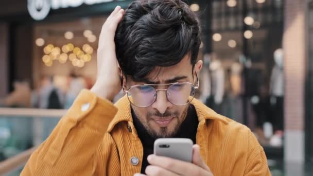 Close-up sad upset shocked young indian man receiving email on smartphone bankruptcy notice feels shock stressed sadness worried about bad news loss failure disappointment refuses to believe problem — Vídeos de Stock