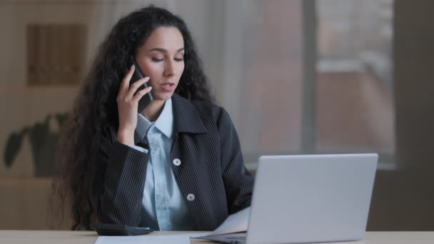Komoly spanyol üzleti nő professzionális vállalkozó főnök munka multitasking beszélni mobiltelefon az irodában nézd meg laptop képernyőn, hogy rendelés távolról csinál papírmunka számítás megerősíteni online honlapján — Stock videók