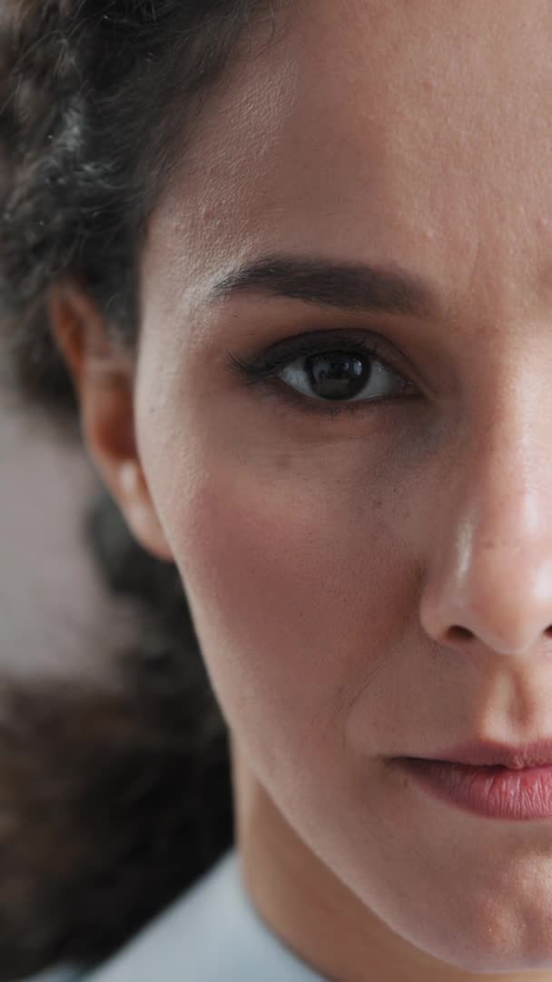 Vertikale Ansicht Halbgesicht Nahaufnahme Porträt von ernsthaften jungen arabischen Frau Angestellte Geschäftsfrau öffnen weibliche Augen stehen drinnen Blick auf Kamera sinnliche hispanische Mädchen mit lockigem Haar natürliches Make-up — Stockvideo