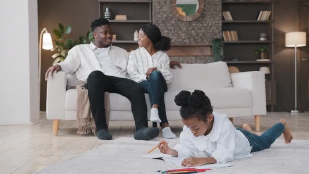 Famiglia africana relax nella nuova casa affittato appartamento proprio appartamento. Genitori casual parlando seduti sul divano in salotto figlia disegno con matite di colore sdraiato sul pavimento. Assicurazione immobiliare prestito — Video Stock