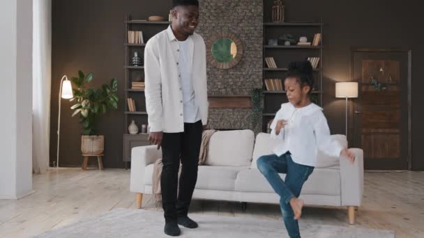 Aktives Familienwochenende zu Hause. Fröhlich lustige Vater afrikanischen Papa und kleine Mädchen Tochter springen im Wohnzimmer tanzen verrückten Tanz Spaß lachen fröhliche Feiertagsfeier unbeschwerte Bewegung — Stockvideo