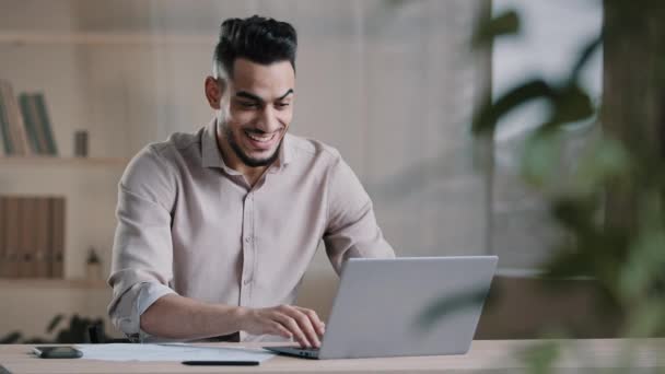 Opgewonden jonge mannelijke Spaanse winnaar zakenman kijk naar laptop scherm typen zakelijke aanbod krijgen commerciële winst zitten op de werkplek dansen dolblij man ontvangen beloning bonus te vieren online loterij — Stockvideo