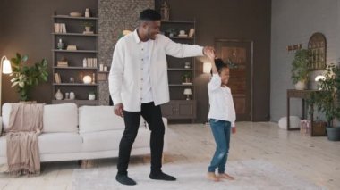 Sevgi dolu Afrikalı Amerikalı baba, küçük bir çocukla el ele tutuşup, küçük kız çocuğuyla dans ediyor. Oturma odasında mutlu baba ve küçük kız, babasıyla dans ederek dönüyorlar.