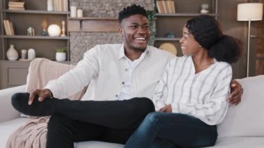 Evli çift Afrikalı erkek ve melez kadın konuşuyor. Yeni evdeki oturma odasında birlikte gülüyorlar. Kendi evlerinde sevgili karı koca muhabbetleri yapıyorlar.