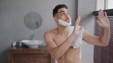 Komik, neşeli, neşeli, neşeli, mutlu, kaygısız, Arap, kaslı, beyaz köpüklü, sakalında jöle olan, dans eden, ritmik dans eden, müzik eşliğinde şarkı söyleyen, tıraş olmadan önce banyoda dans eden çıplak adam.