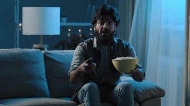 Akşamları evdeki karanlık oturma odasında Arap sakallı bir adam oturur ve TV 'de televizyon seyreder. İnternetteki spor şampiyonası programı işten sonra gevşeyen patlamış mısır yer. 