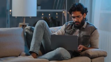 Serbest çalışan Arap Hintli adam, gece geç saatlerde gözlüklü, sakallı erkek kullanıcı. İnternette dizüstü bilgisayarla oturup haberleri okuyor.