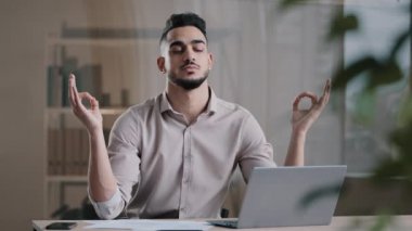 Sakin Arap iş adamı profesyonel işçi gözleri kapalı iş yerinde meditasyon yapıyor stresi görmezden geliyor yoga yapan barışçıl erkek patron için nefes alıyor iş yerinde zen dengesi kuruyor