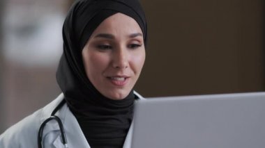 Gülümseyen Arap İslami kadın cerrah kadın cerrah kadın tesettür sanal sohbette uzaktan yardım sağlamak için çevrimiçi danışmanlık yapın kısmen video konferans tıbbi teletıp alın