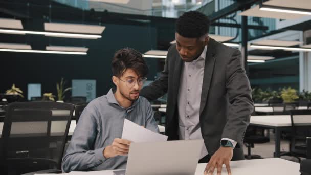 Male african mentor financial advisor businessman boss helping arab man colleague discussing marketing result in report paperwork american supervisor training partner giving business advice at office — Stock Video