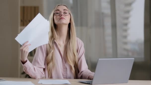 Caucasian tired sad woman sit at desk in office suffer from heat cools herself with documents papers feel unwell high temperature in room without air-conditioning system summer work hormonal imbalance — Vídeos de Stock