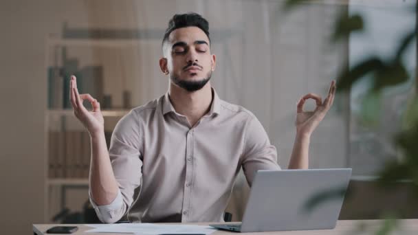 Спокойный арабский бизнесмен профессиональный работник глаза закрыты принимая перерыв медитируя на рабочем столе игнорируя стресс дыхание для спокойного ума мужской босс делает йогу поза чувство дзен баланс на рабочем месте — стоковое видео