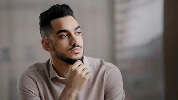 Düşünceli, ciddi, genç, İspanyol asıllı, şüpheli, profesyonel bir erkek, ofis masasında oturuyor. Başını çevirmiş, düşüncelere dalmış, yeni bir fikir arıyor. Zor bir karar ver.