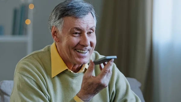 Yetişkin, gri saçlı, 60 'lı yaşlarda yaşlı bir erkek. Akıllı telefonu tut. Mikrofon hoparlörüne yüksek sesle konuş. — Stok fotoğraf