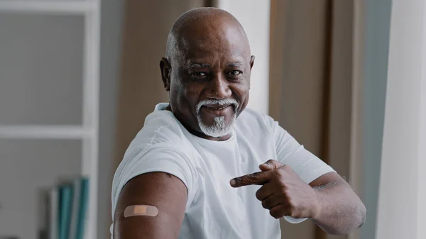 Portrait african american old senior mature man patient shows medical plaster on shoulder demonstrates injection mark satisfied male client after vaccination with covid-19 virus vaccine antivirus dose — Stok fotoğraf