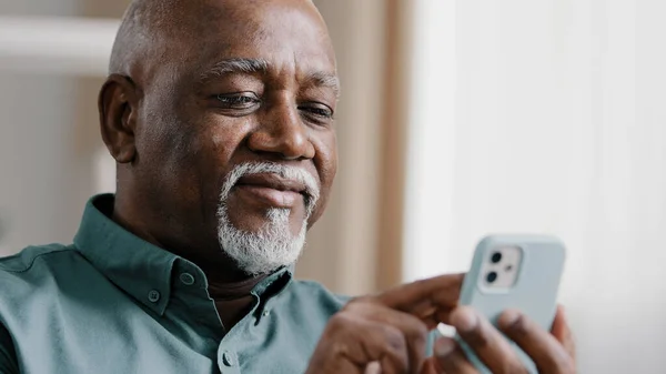 上了年纪的非洲60多岁的男子使用电话，美国商人，男性祖父免费无线网络聊天移动应用在家里上网发短信在智能手机互联网技术 — 图库照片