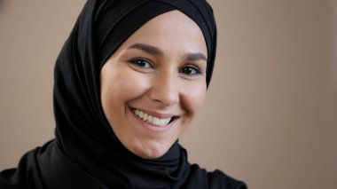 Close up face portrait of young pretty 30s muslim islamic arab woman model wearing traditional hijab headscarf confident posing looking at camera dental smiling feeling well satisfied with good vision