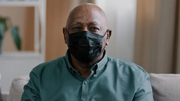 Portrait old lonely african dominican mature man 60s grandfather mature senior male sad pensive patient in black medical mask at home indoors looking at camera isolation covid coronavirus pandemic — Foto Stock