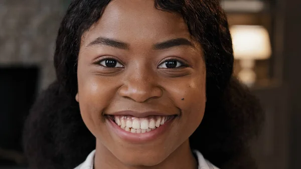 Extreme close up female face with perfect skin healthy millennial african woman looking at camera indoors happy 20s 30s girl with white toothy smile in apartment smiling casual model posing portrait — Stock Photo, Image