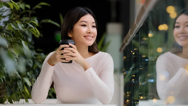 Asian girl woman smiling enjoying drinking fragrant delicious coffee hot tea morning cappuccino in cafe sitting at table smiling waiting for meeting relaxing on break resting in cafeteria weekend — Stock Photo, Image