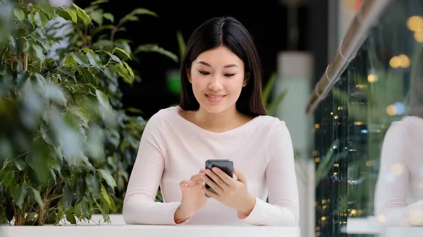 Asiatique coréen fille utilisateur pigiste joueur femme assise dans un café à table au bureau avec téléphone se réjouissant de la victoire gagner jeu mobile succès offre message succès paiement gagner — Photo