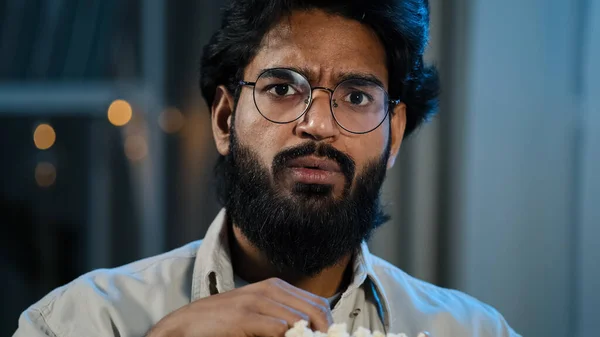 Male home portrait serious interested attentive Arabic Hispanic Indian bearded man guy in glasses eating popcorn watching TV show series late evening night watch movie online sport game championship — Foto Stock