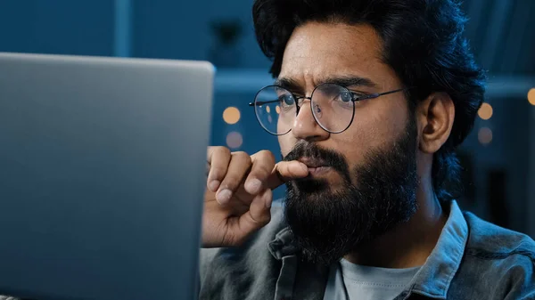 Focused Arabian Indian bearded man freelancer in eyeglasses working on computer at home late night looking in screen searching decision feels doubt creating online project thinking on problem solution — Stockfoto