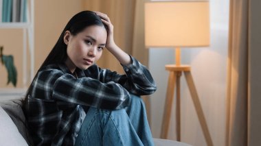 Yalnız, yorgun, bıkkın, üzgün, Asyalı, yorgun, yorgun bir kadın. Evdeki koltukta oturan, kendinden emin olmayan, mutsuz, mutsuz, kötü, ruhsal sorunları olan, depresyonda, umutsuz, düşünceli Koreli bir kız.