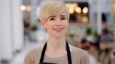 Yakın plan bayan kahveci. Portre garsonu, beyaz, orta yaşlı, kısa saçlı, dişlek, gülümseyen kameraya bakan sarışın kadın. Kafeterya Kafeterya Bar 'da çalışan kadın çalışan.