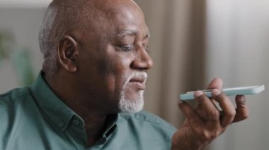 Olgun, gri saçlı, 60 'lı yaşlarda, sakallı, çift ırklı, Afrikalı, Amerikalı, yaşlı, akıllı telefonlu, akıllı, hoparlörlü, konuşan, cep telefonu uygulaması kullanarak ses hoparlörüne konuşan yaşlı bir adam.