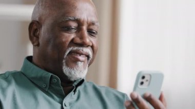 Yetişkin yaşlı Afrikalı 60 'lı yaşlarda çift ırklı bir adam. Amerikan iş adamı, erkek, büyükbaba, internet üzerinden akıllı telefon teknolojisiyle internet mesajlaşması yapan internet uygulamasında ücretsiz kablosuz sohbet uygulaması kullanıyor.