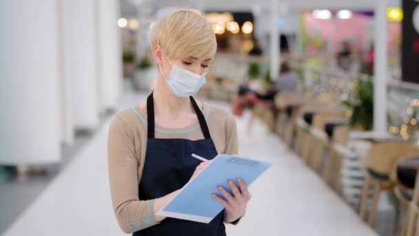 Närbild kaukasisk medelålders kvinna cafeteria restaurang arbetare servitris i medic ansikte mask skriva med penna ta emot order i cafe pandemi professionell manager dam skriver på papper småföretag — Stockvideo