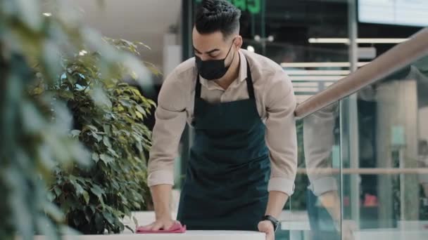 Arabe homme travailleur hispanique garçon serveur dans masque médical traiteur dans tablier essuie table éclaboussures avec désinfectant fait le nettoyage avant l'ouverture restaurant prépare café pour les visiteurs ouverts travaux — Video