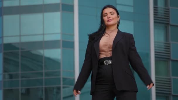Fiatal sikeres, elegáns spanyol üzletasszony üzleti öltönyben áll magabiztos pózban karokkal keresztbe tett irodaházzal a háttérben érzés siker szabadság teljesítmény pózol szabadban — Stock videók
